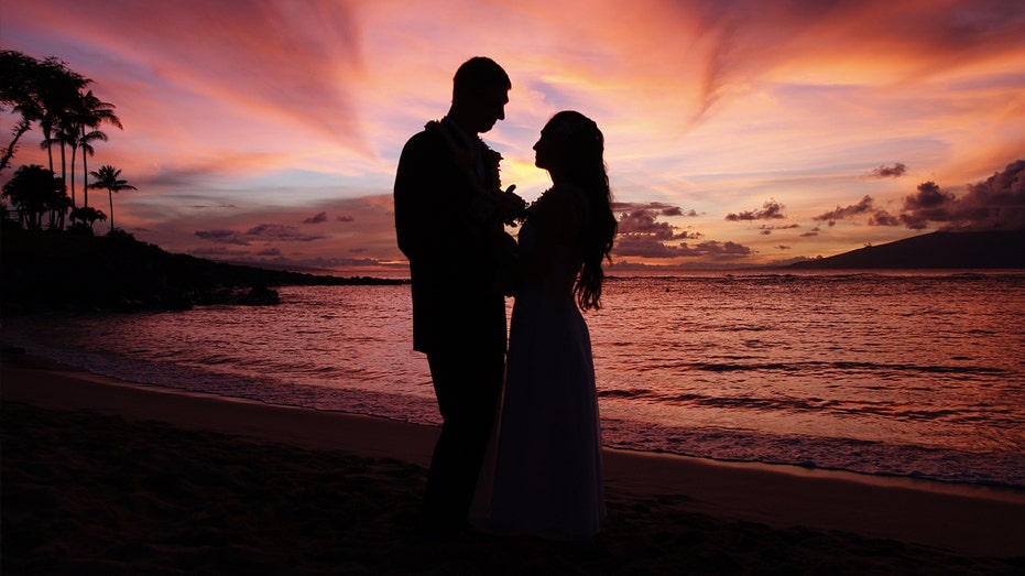 Couple on a beach in Maui face each other at sunset.